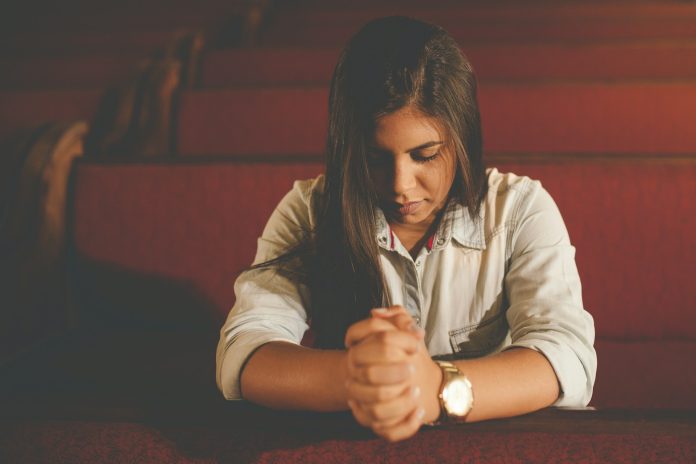 Mulher brasileira em oração dentro de uma igreja durante reflexão sobre feminismo e cristianismo