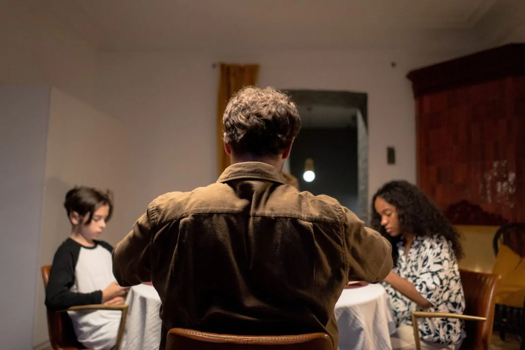 Pai sentado à mesa com os filhos em momento de convivência familiar