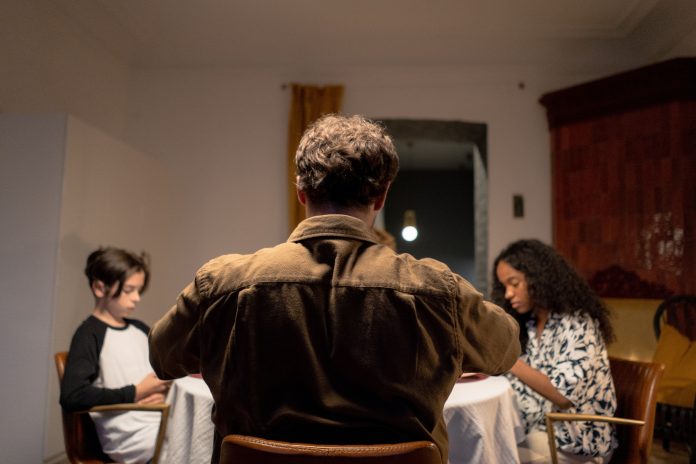 Pai sentado à mesa com os filhos em momento de convivência familiar