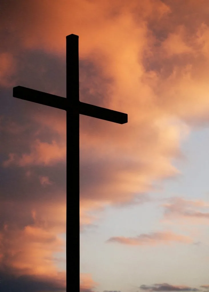 Existe voto cristão? O perigo de usar a Bíblia pela metade Silhueta de uma cruz diante de um céu alaranjado ao pôr do sol.