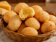 cesta em uma mesa de madeira com várias bolinhas de pão de queijo e uma partida ao meio