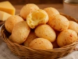 cesta em uma mesa de madeira com várias bolinhas de pão de queijo e uma partida ao meio